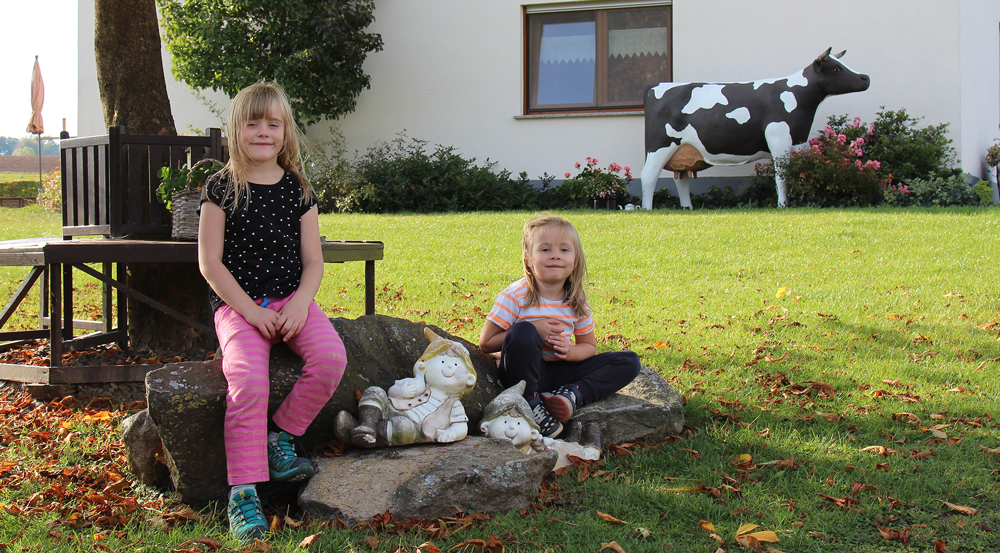 Kinder sitzen im Garten vor dem Bauernhof